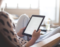 Symbolfoto Benutzung eines Tablets Person sitzt in einem Sessel und hält ein Tablet mit Textanzeige in den Händen.