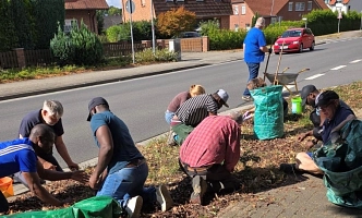 Eine Gruppe von Menschen kniend und hockend bei der Gartenarbeit auf dem Grünstreifen an der B 188 in Osloß.