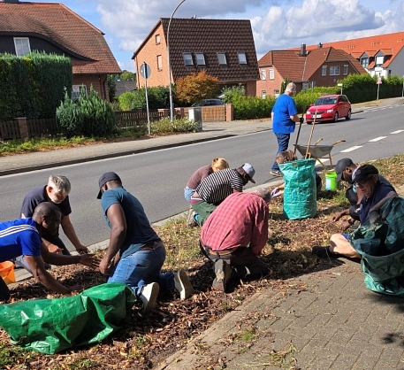 Eine Gruppe von Menschen kniend und hockend bei der Gartenarbeit auf dem Grünstreifen an der B 188 in Osloß.